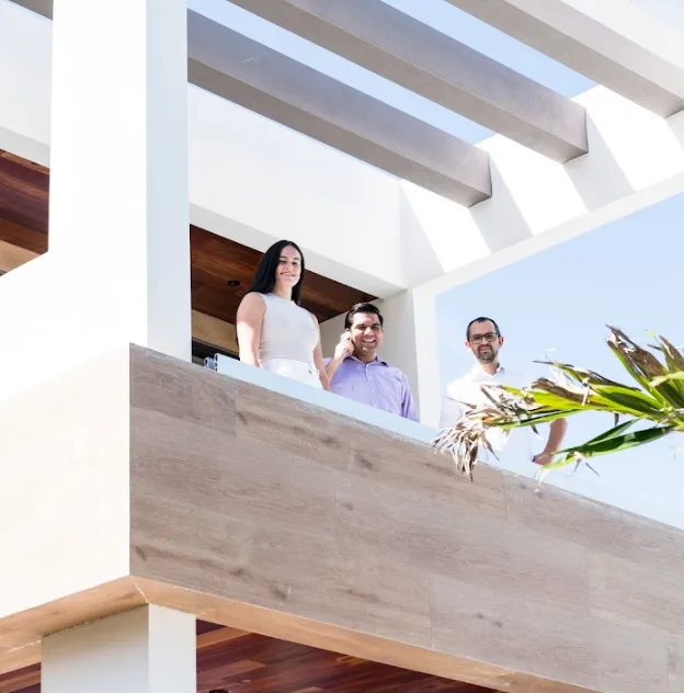 This is an image of three members of the AGD team, luxury real estate developers in Miami. They are on a sun-soaked balcony of a modern-style luxury home. They are happy and are overlooking the property with confidence.
