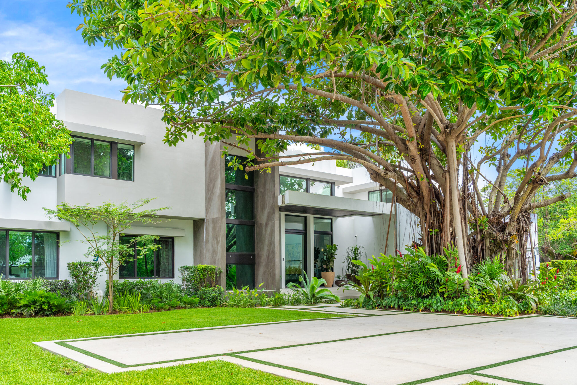 Pincrest Luxury Home This is an image of a modern style luxury home with concrete slab approach and a large tree in the front yard. This project exemplifies the holistic approach delivered by a female real estate developer.