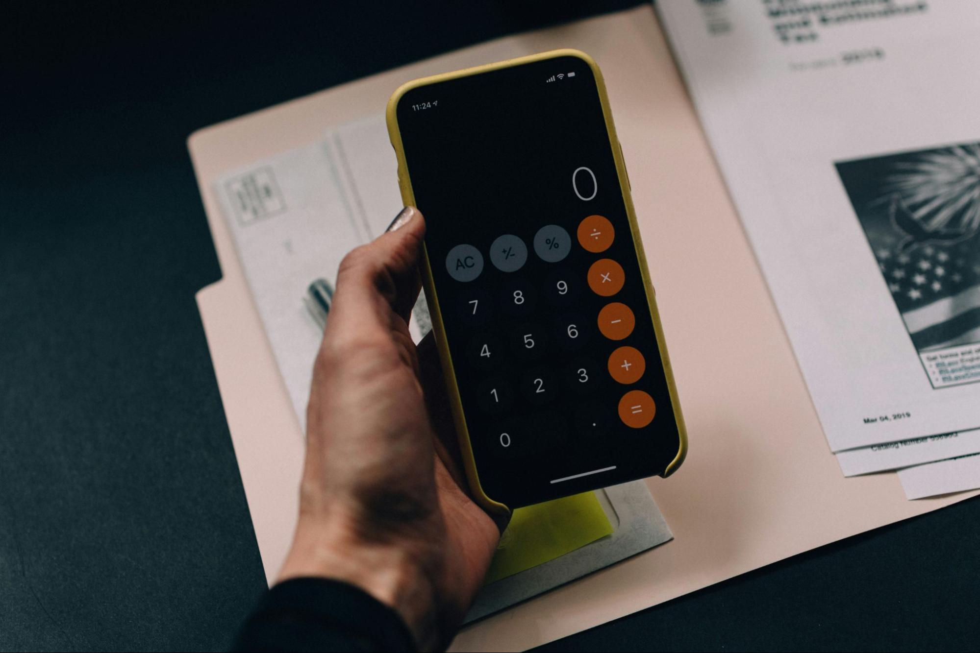 a calculator is held above a folder with some real estate documents in it. Calculations for ROI with a real estate investment trust can be difficult because of volitility.